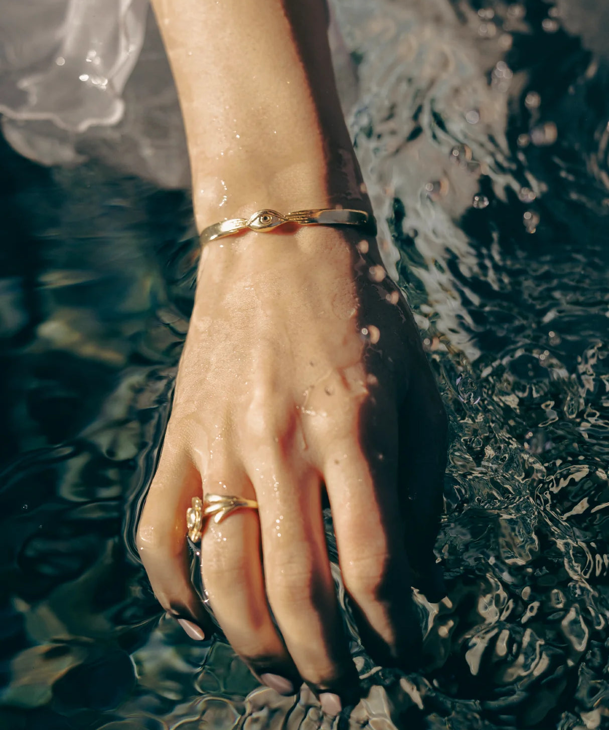 Hand with gold bracelet and ring touching water