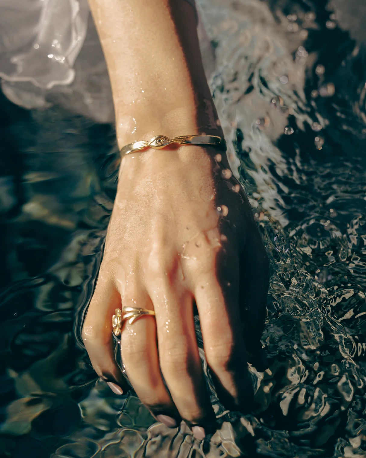 Hand with gold bracelet and ring touching water