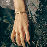 Hand with gold bracelet and ring touching water